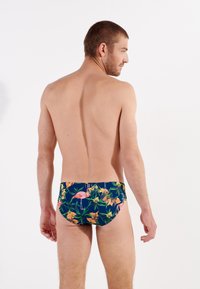 Herren-Schwimmslips mit einem navyblauen Grundton und einem bunten Blumen- und Flamingo-Muster. Der Stoff ist glatt und sorgen für eine taillierte Silhouette.