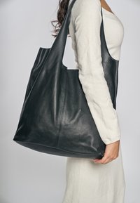 Duża czarna torba na ramię ze skóry o teksturowanym wykończeniu, wyposażona w dwa długie uchwyty i minimalistyczny design, przedstawiona na jednolitym tle.