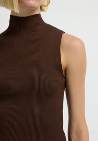 Bruine geribbelde mouwloze top met een hoge hals, met kleine metalen accenten door de stof heen, en een aansluitende silhoeet.
