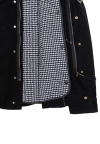 Zwarte jas met een gestructureerde buitenkant, voorzien van een houndstooth patroon voering in wit en zwart. Inclusief drukknoopsluitingen en ritsen.
