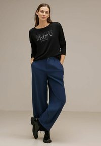 Camicia nera a maniche lunghe con grafica "inspire", abbinata a pantaloni larghi blu scuri e scarpe stringate nere. Tessuto con una texture liscia.