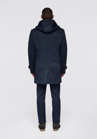 Navy coat with a high collar and hood, featuring a streamlined design and smooth texture; paired with matching navy pants and brown footwear.