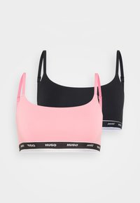 Deux bralettes en rose et noir, dotées d'un tissu lisse, de bretelles ajustables et d'une ceinture noire contrastante avec le logo "HUGO".
