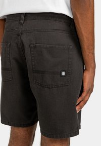 Zwarte denim shorts met twee achterzakken en een logo-patch. De tailleband heeft een standaardhoogte met een rechte snit en toont een gladde textuur.