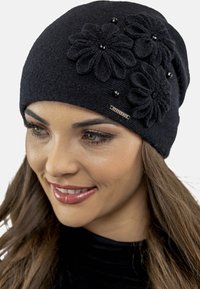 Black knitted beanie featuring three textured flower appliqués with black bead accents and a small metal tag on the side.