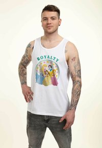 Top de tirantes blanco con un gráfico colorido de cinco princesas bajo la palabra "REINALEZA", rodeado por un borde floral redondo. Jeans de mezclilla y tatuajes visibles.