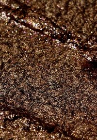 Material marrone lucido con superficie texturizzata, caratterizzato da riflessi dorati e ramati. I motivi irregolari creano riflessi di luce variabili.