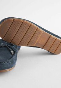 Navy suede mokasinikenkiä, joissa on kumipohjat, joissa on yksityiskohtaiset kuvioinnit ja koristeelliset nauhat. Hienovaraiset ommeltu korostukset lisäävät tekstuuria.