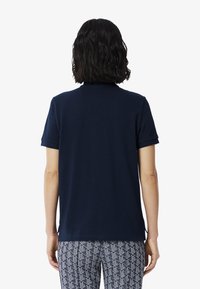 Tummansininen polo-paita, jossa on lyhyet hihat ja klassinen kaulus. Paidassa on sileä pinta ja huomaamattomat sivureiät helmassa.