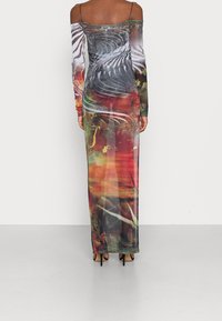 Robe longue moulante avec décolleté dénudé, en tissu transparent affichant des motifs abstraits colorés en rouge, vert, noir et blanc.
