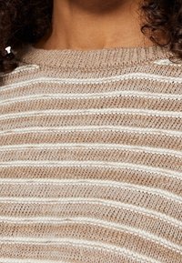 Beżowy sweter robiony na drutach z białymi poziomymi paskami, posiadający teksturowany wzór i okrągły dekolt. Miękki materiał o przytulnym wyglądzie.