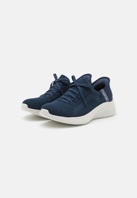 Baskets de sport bleu marine avec une tige en maille texturée, une semelle en caoutchouc blanche et un système de laçage. Présente des rayures discrètes et des accents de rembourrage.