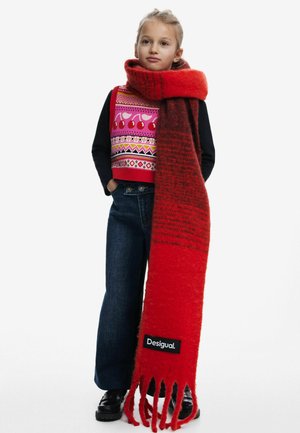 Écharpe en laine rouge avec des extrémités à franges et une étiquette noire "Desigual" ; présente un dégradé du rouge foncé au rouge vif, portée de manière décontractée sur un haut à motifs.