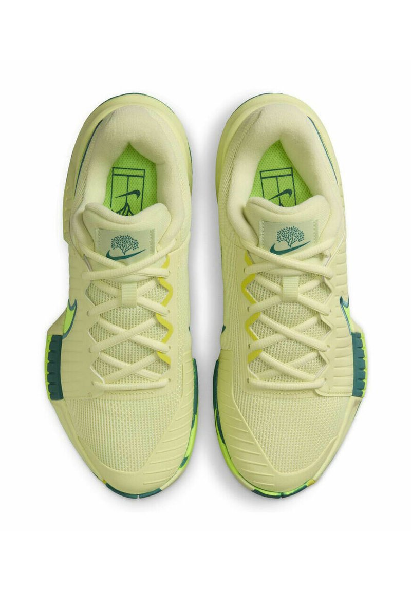 Baskets de sport jaune clair avec un dessus en maille, des accents verts, une semelle texturée et un design lacé. Présente un logo sur la languette et sur le côté.