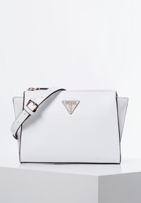 Biała skórzana torba na ramię z trójkątnym złotym logo, kontrastującymi brązowymi akcentami, regulowanym paskiem i kanciastym designem. Gładka faktura.