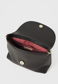 Černá kožená taška s texturovaným povrchem, zlatým zapínáním na cvok a vínovým interiérem obsahujícím více přihrádek a štítek.