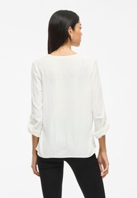 Hvid, struktureret bluse med trekvartærmer, rund halsudskæring og opsmøgte manchetter, parret med sorte slim-fit bukser.