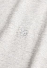 Lysegråt stof med subtil tekstur og små, syede monograminitialer "DC" i matchende gråt tråd i midten.