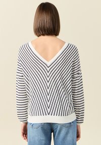 Wit en marineblauw gestreepte trui met een V-vormige rug, lange mouwen en geribbelde zoom. De stof heeft een textuurpatroon met zigzag lijnen.