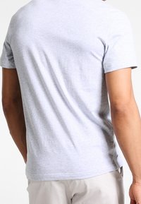 Graues Baumwoll-T-Shirt, Rundhalsausschnitt, kurze Ärmel, glatte Textur, minimalistisches Design, mit einem kleinen Logodetail in der Nähe des Saums.