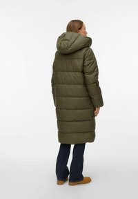 Oliiviroheline sulejope kapuutsiga, tikandiga ja pikkade varrukatega, ulatudes poolde vasikka, kombineeritud tumeliste siniste teksadega.