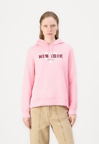 Felpa rosa con tasca frontale, caratterizzata dalla scritta "NEW YORK" in lettere grasse e un design a forma di cuore. Manicotti e orlo a coste, realizzata in materiale morbido.