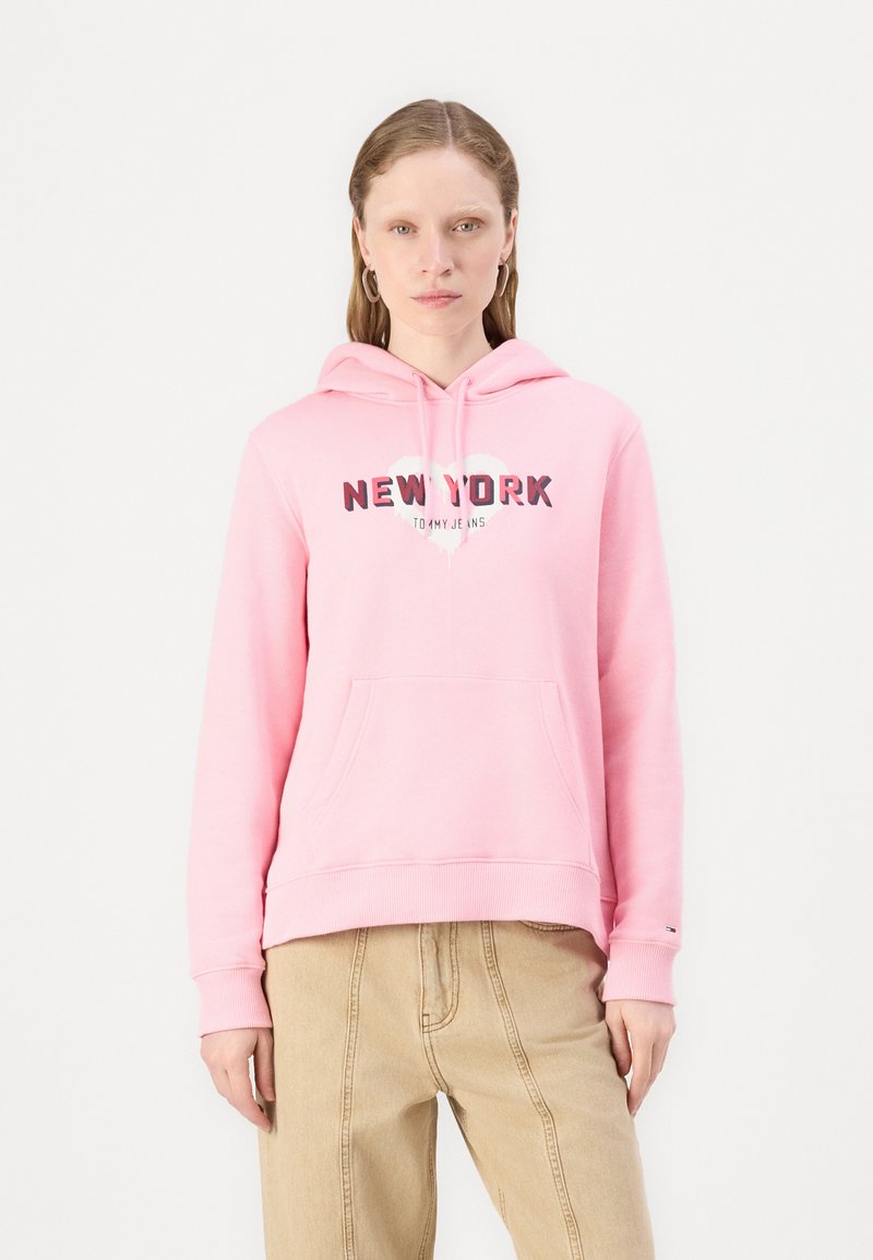 Felpa rosa con tasca frontale, caratterizzata dalla scritta "NEW YORK" in lettere grasse e un design a forma di cuore. Manicotti e orlo a coste, realizzata in materiale morbido.