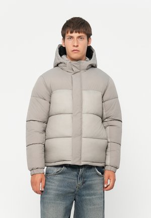 Padded grey jacket with a hood, featuring a quilted design, elastic cuffs, and a front zip closure, worn over distressed jeans.