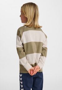 Grön- och krämrandig långärmad skjorta med avslappnad passform, texturerat tyg och ribbade ärmslut, kombinerad med marina byxor med ett chevronmönster.