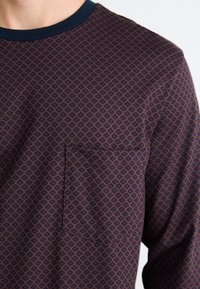 Chemise à manches longues dans des tons bleu foncé et bordeaux, avec un motif géométrique en losange, un col rond bleu marine et une poche poitrine.