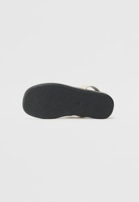 Black rubber sole with textured grip pattern; beige straps made of smooth material, featuring minimalistic design with no additional accents.