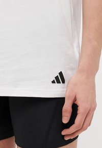 Λευκό βαμβακερό t-shirt με κοντά μανίκια, διακοσμημένο με ένα μαύρο λογότυπο με τρεις ρίγες στο κάτω μέρος. Φορώντας το με μαύρες βερμούδες, αποτυπώνει μια λεία υφή.
