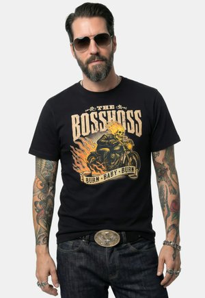 Mand med skæg og solbriller iført en sort T-shirt med motiv af en flammet kranierider på motorcykel med teksten "The Bosshoss Burn Baby Burn."