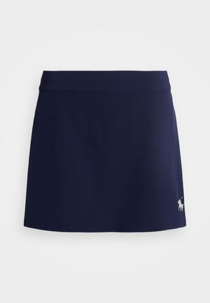 Skort azul marino hecho de un tejido suave, con una cinturilla ajustada y un dobladillo alargado, acentuado por un sutil logo en la esquina inferior izquierda.