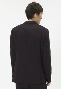 Sacou de culoare mov închis, cu o deschidere la spate, rever în formă de fanteză și detalii cu mâneci butonate, realizat dintr-un material fin.