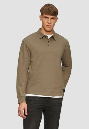 Olijfgroene polo met lange mouwen, een kraag, een knoopsluiting en geribbelde manchetten, gecombineerd met donkere jeans.
