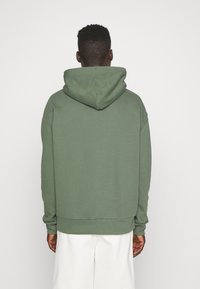 Felpa verde con una vestibilità comoda, dotata di un grande cappuccio e polsini a coste. La parte posteriore è liscia con un design semplice e senza decorazioni.