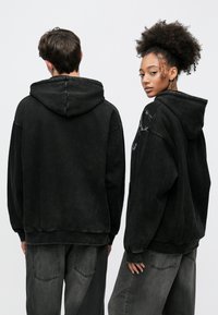 Μαύρα oversized φούτερ με ματ υφή, που διαθέτουν τσέπη καγκουρό και ριμπ μανσέτες, συνδυασμένα με σκούρα γκρι φαρδιά τζιν.