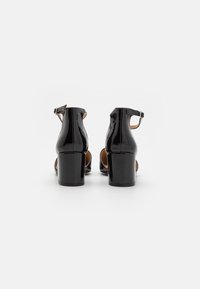 Sandalias de tacón alto de charol negro con tira en el tobillo, diseño abierto, tacón grueso y textura suave.