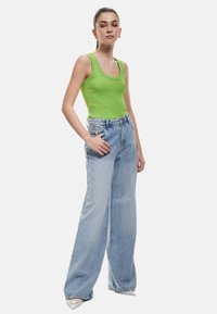 Top giallo rigato abbinato a jeans in denim azzurro chiaro a gamba larga. La modella si presenta con una mano in tasca, mostrando un look semplice e rilassato.