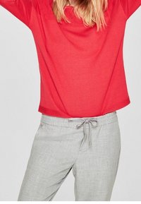 Pull léger rouge avec une coupe décontractée et des détails côtelés, associé à un pantalon gris clair avec cordon de serrage et une texture subtile.