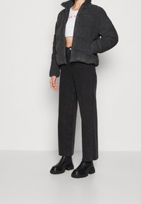 Svart kordflöjls puffjacka med hög krage, kort passform och dragkedjestängning, i kombination med högmidjade svarta jeans och kraftiga svarta stövlar.