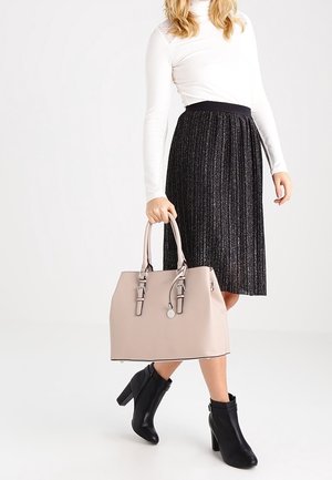 Beżowa torebka z podwójnymi uchwytami i srebrnymi akcentami, o wyraźnym kształcie, umieszczona na tle osoby w białej bluzce i plisowanej czarnej spódnicy.