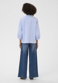 Cămașă în dungi albastre deschis și albe cu mâneci bufante, asortată cu blugi denim cu picioare largi. Ambele articole vestimentare au un design casual.