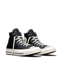 Paire de baskets montantes en toile noire avec semelles en caoutchouc blanc et lacets, disposées légèrement en angle sur un fond blanc.