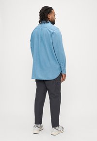 Jasnoniebieska koszula zapinana na guziki, wykonana z denimu, z długimi rękawami, o casualowym kroju, z zaokrąglonym dołem, noszona z ciemnymi spodniami bojówkami i jasnymi tenisówkami.