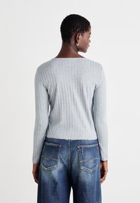 Lys grå ribbestrikket langermet topp med en tettsittende design, paret med løse blå denimjeans med doble baklommer og kontrastsømmer.