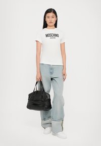 White cotton t-shirt with "MOSCHINO JEANS" black lettering, paired with light blue oversized denim jeans and a black handbag with gold accents.
