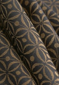 Nahaufnahme eines schwarzen Stoffes mit einem goldenen geometrischen Blumenmuster und sichtbarer gewebter Textur, der in sanften Falten gezeigt wird.