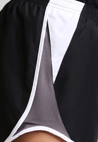 Lähikuva mustista urheilushorteista, joissa on valkoinen reunus ja harmaa verkko sisäkerros. Korostuu sivuaukkojen muotoilu ja joustava vyötärönauha.